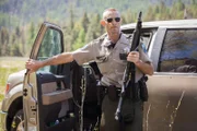 Officer McCormick stepping out of a car with his gun to scare the Black Bear away.