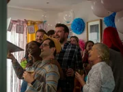 Denise (Jennifer Heylen, vorne l.) und Lloyd (Stephen Jones, hinten l.) feiern mit Freunden und Familie eine Party, auf der sie das Geschlecht ihres noch ungeborenen Kindes bekannt geben.