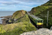 Der DART lässt die letzte Klippe hinter sich liegen: Der Nahverkehrszug zwischen Greystones und Bray fährt auf eingleisiger Strecke. Parallel zur Bahn verläuft ein Spazierweg, der Cliff Walk.