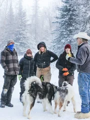 Marty (r.) unterhält sich mit (v.l.n.r.) Maciah, Gauge, Misty und Mollee im Schnee, während zwei Hunde in der Nähe sind.