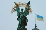 Statue in Lwiw mit ukrainischer Flagge im Hintergrund.