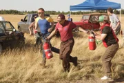 Eine Gruppe von Männern beobachtet entsetzt, wie Flug 143 auf das Rollfeld rutscht, und eilt sofort mit Feuerlöschern herbei