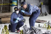 An Investigator holds up a piece of debris while another Investigator photographs  and documents the debris as evidence