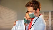 Lisa (Marie Seiser, l.) ist total erschöpft, Dr. von Hatzfeld (Tom Radisch, r.) nimmt sie in den Arm. Sie wurden von einem plötzlichen Ansturm auf die Praxis überrascht. In einem Wettrennen gegen die Zeit versuchen sie hinter die Ursache der mysteriösen Erkrankung zu kommen und die Quarantäne zu beenden.