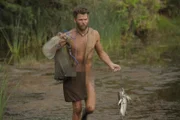 Steven geht mit seinem Fischernetz, seiner Tasche und einem Fisch in der Hand am Flussufer entlang.