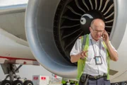 DUBAI - Leigh Faulkner, Emirates Line Maintenance engineeer, on the phone in front of an aircraft engine.