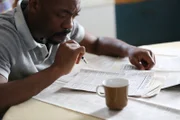 Nathaniel looks over classifieds articles to find a job.