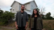 Hosts Nick Groff and Katrina Weidman stand in yard with Monroe Demon House in hill behind them.