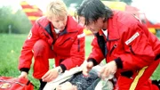 Berger (Serge Falck, l.) und Dr. Lüdwitz (Rainer Grenkowitz, r.) treffen am Unfallort ein und versorgen den verletzten Troger (Christian Oskar Spitzl). Was sie nicht ahnen: Seine Tochter verzweifelt in einem führerlosen Fesselballon am Himmel...