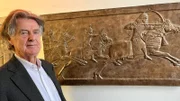 Ein Mann steht vor einem Museumsexponat, das Aschurbanipal, den assyrischen König von 668-627 v. Chr., darstellt. Auf der Jagd nach einem Löwen. Entdeckt im assyrischen Palast in Ninive.
