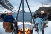Die Moderatoren Monica Galetti und Rob Rinder wärmen sich an der Feuerstelle im Nusfjord Arctic Resort, Norwegen auf.