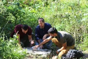 Justin Fornal, Paul Lindscot, and Emiliano Ruprah examining a petroglyph map of the cavern in Sulphur Springs, Arkansas. They are pouring water on the rock to see the carved-in lines more clearly.