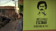 Doug Laux leans against a wall in the barrio with a stencil of Pablo Escobar's face spray-painted on its surface.