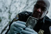 Rekonstruktion eines Dramas: Männlicher Polizist hält ein zertrümmertes Telefon