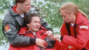 Dr. Karin Thaler (Roswitha Meyer) untersucht den bei einem Schusswechsel lebensgefährlich verletzten Dr. Lüdwitz (Rainer Grenkowitz). (li.: Manfred Stücklschwaiger als Thomas Wächter)