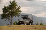 Wide shot of a tree with a truck where Jerry, Colin, Max, and Guillermo are looking at a computer.