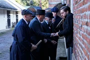 Eine Gruppe von Menschen nähert sich einem Mann, der am Eingang eines Hauses steht.