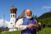"Klingendes Österreich", "Der Untersberg und die Sage vom Kaiser Karl." Vom Untersberg bei Salzburg muss wahrhaftig ein großer Zauber ausgehen. Kein anderer Berg weitum ist mit Sagen, Legenden, Kraftplätzen und wundersamen Dingen so angefüllt wie er. Sepp Forcher war da oben acht Jahre lang - Sommer und Winter - mit seiner Familie als Hüttenwirt daheim. Was liegt darum näher für ihn, als seinen ehemaligen Heimatberg wieder einmal zu besuchen und den alten Zeiten und Sagen nachzusinnen, wobei die Sage vom Kaiser Karl einen ganz besonderen Platz einnimmt. Dabei musizieren und singen: Elstätzinger Musikanten, Weißenbacher Tanzlmusi, Junge Ramsauer Sänger, Harfenduo Steiner-Schroll, Rotofenmusi, Lockstoa-Musi, Wiesberger Dreigesang, Trachtenmusikkapelle Wals und Historische Landwehrschützen Wals. Im Bild: Sepp Forcher bei der Kirche in Oberau.