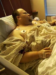 Chad in the hospital bed post surgery with his wife Ayesha and daughter Taque.