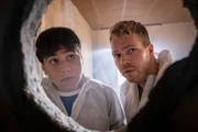 Ernst Hakke (Diyar Ilhan, l.) und Julian Beil (Ben Münchow, r.) blicken durch ein Loch in der Wand: Eine unerwartete Entdeckung sorgt für Verwunderung während der chaotischen Wohnungsrenovierung.