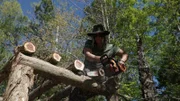 Misty Raney chain sawing a log of wood whilst sitting on the roof.