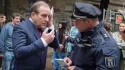 Jörg Hanke (Uwe Preuss, l.) kühlt sein Auge und spricht mit einem Polizisten (Komparse).
