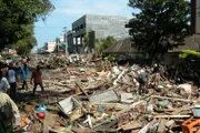 Überlebende gehen durch die Trümmer, die die Straßen nach dem Tsunami in Banda Aceh, Indonesien, füllen. Ein schweres Erdbeben im Indischen Ozean löst einen Tsunami aus, der innerhalb von Minuten die belebte Stadt Aceh erreicht und eine noch nie dagewesene Verwüstung anrichtet.