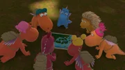 Auf dem Waldboden kniend, sind der kleine Drache Drache Kokosnuss und seine Freunde konzentriert über eine Landkarte gebeugt.