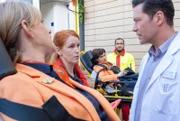 Dr. Philipp Brentano (Thomas Koch, re.) nimmt Nicole Marburger (Judith Richter, li.) und Elsa Sommer (Naemi Florez, 3.v.re.) von der Notärztin entgegen. Die beiden Flugbegleiterinnen hatten Streit, der mit dem Riss der Achillessehne bei der einen und dem Verdacht auf ein Schädel-Hirn-Trauma bei der anderen endete.