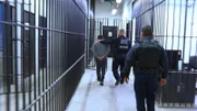 Polizisten begleiten einen Mann im Gefängnis.