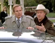 Sheriff Mort Metzger (Ron Mazak) verhört den Privatdetektiv Charlie Garrett (Wayne Rogers), der überraschenderweise in Cabot Cove aufgetaucht ist.