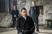Nachdem ein kleines Mädchen aus ihrem Haus entführt und ihr Vater ermordet wurde, hoffen Holmes (Jonny Lee Miller, M.) und Capt. Gregson (Aidan Quinn, r.), im Gefängnis etwas von Moriarty darüber zu erfahren. Moriartys Aufpasser Agent Mattoo (Faran Tahir, l.) behält die Gefangene dabei stets im Auge ...