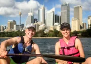 Reiseleiter Moritz und Entertainment-Managerin Maika posieren beim Kayak-Fahren mit Schwimmwesten und Kappen bekleidet vor der Skyline von Sydney, Australien.