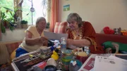 Dagmar (59, re.) bekommt Besuch von Elke (69). Diese ist auf der Suche nach einer barrierefreien Wohnung und erhofft sich Unterstützung von ihrer Freundin.