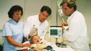 Dr. Stefan Frank (Sigmar Solbach, r.), Dr. Thomas Reinhardt (Christopher Barker) und Oberschwester Charlotte (Barbara Schroth) versorgen den kleinen Sven (Christoph Dirscherl).
