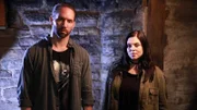 Hosts Nick Groff and Katrina Weidman stand in front of basement brick wall.