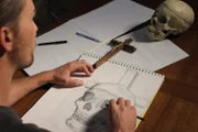 Nick sketching drawings of a skull at the table.