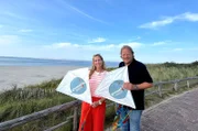Mit den „Grenzenlos köstlich“-Drachen: Tamina Kallert (l) und Björn Freitag fragen sich, ob der Wind stark genug ist, um sie steigen zu lassen.