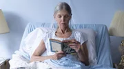 Grandmother reading her book in bed. Sitting alone.