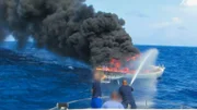 Ein Renn-Segelboot steht auf hoher See in Flammen.