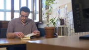 Ein Mann sitzt an einem Tisch und liest ein Buch.