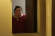 Sarah looks at herself in the mirror.