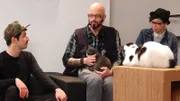 Jackson Galaxy petting a cat in the cafe with staff.