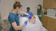 Mid shot of Dr Emma injecting Harley’s ear Keloid before surgery. Nurse Mottie and Nurse Rosie in background..