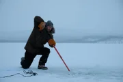 Johnny Rolfe schneidet Löcher ins Eis, um ein Fischernetz unter dem zugefrorenen See auszulegen (National Geographic/Mike Fennell).