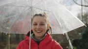 Marina steht bei Regen unter einem Regenschirm.