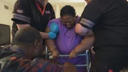 Marla attempting to stand with the help of medics.