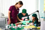 Elisabeth "Betty" Hertz (Henrike Hahn, l.) unterstützt Dr. Julius Walden (Constantin Lücke, M.) dabei, der kleinen Jonna Herdinger (Soraya Maria Efe, r.) zu erklären, wie eine OP funktioniert.