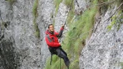 Bear Grylls holds onto rope preparing to abseil pendulum over rock face.