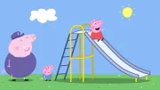 Opa Wutz (l.) ist mit Peppa und Schorsch auf dem Spielplatz und schaut Peppa (r.) beim Rutschen zu.